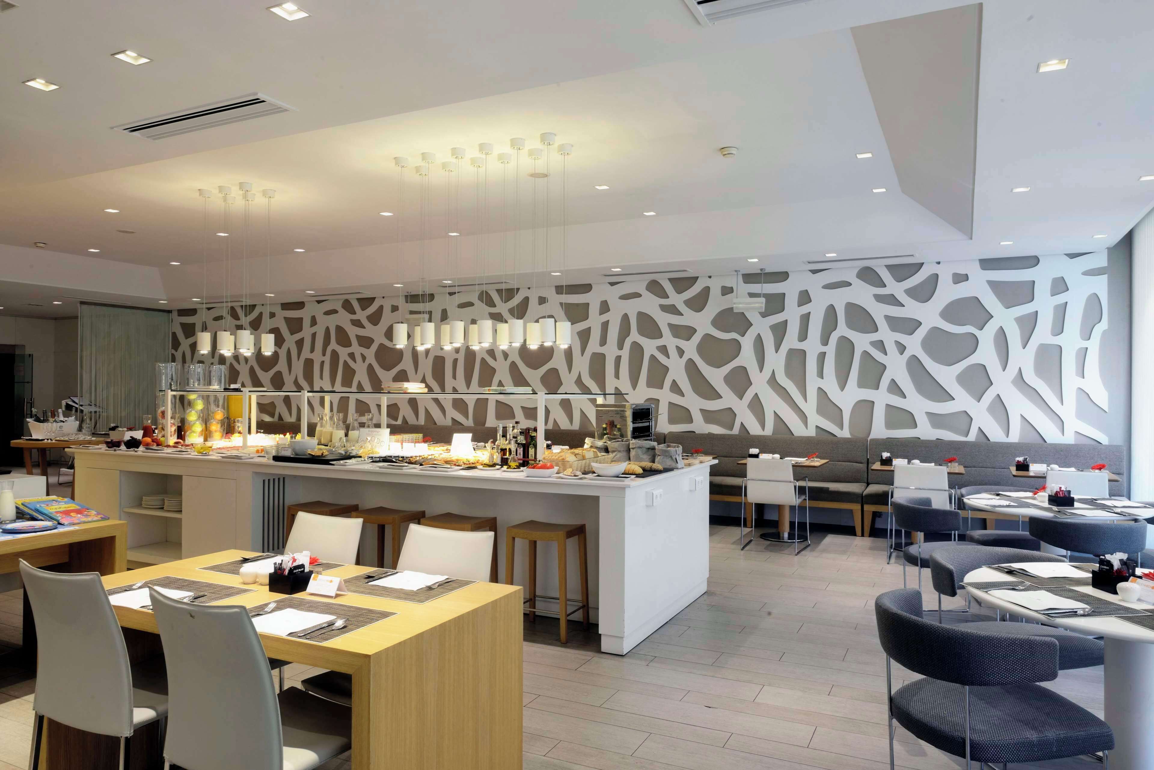 Un restaurante moderno con una isla central, varias zonas de estar y una pared decorativa.
