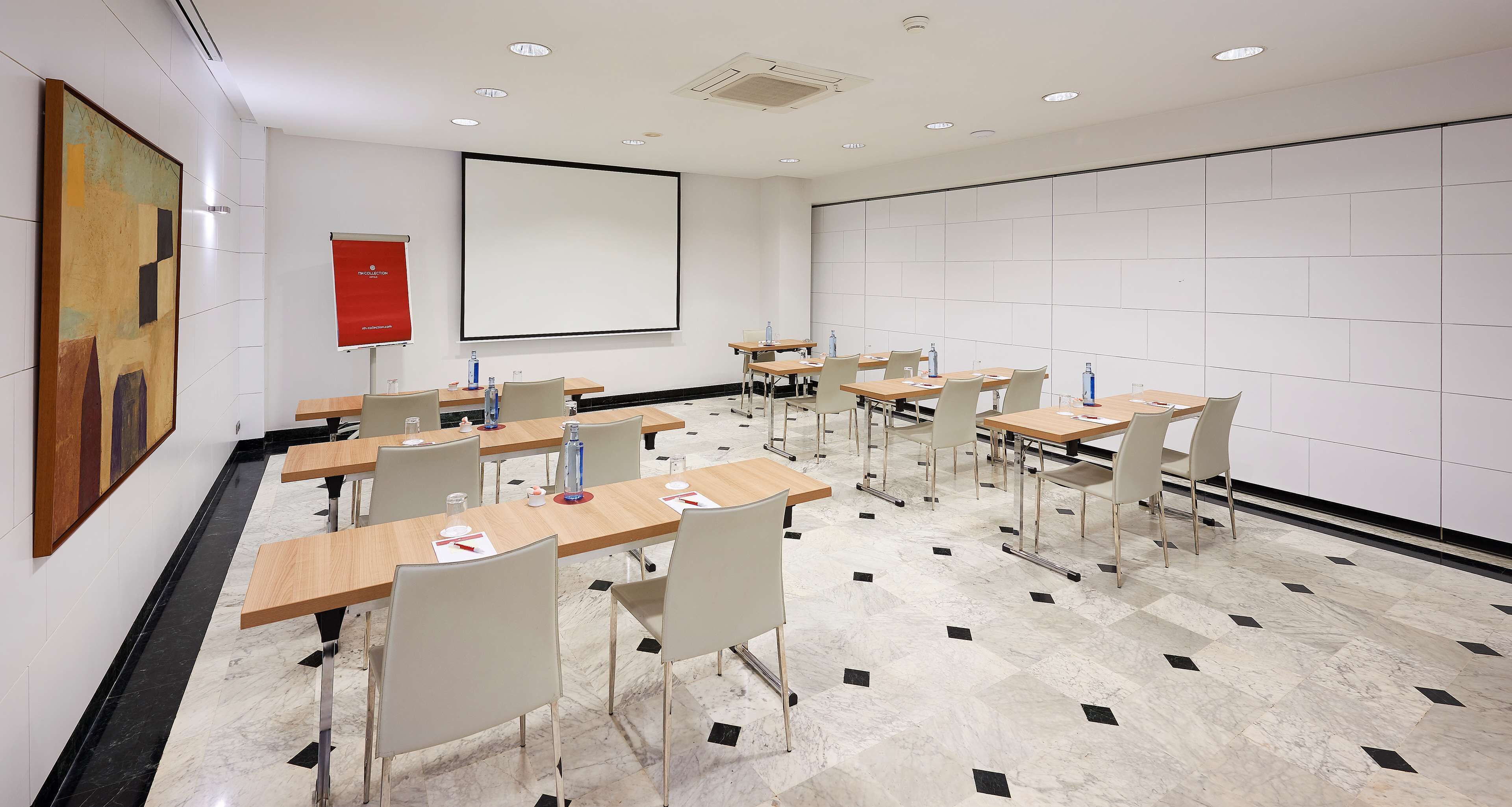 A conference room with a large projection screen, multiple tables with chairs, and a tiled floor.