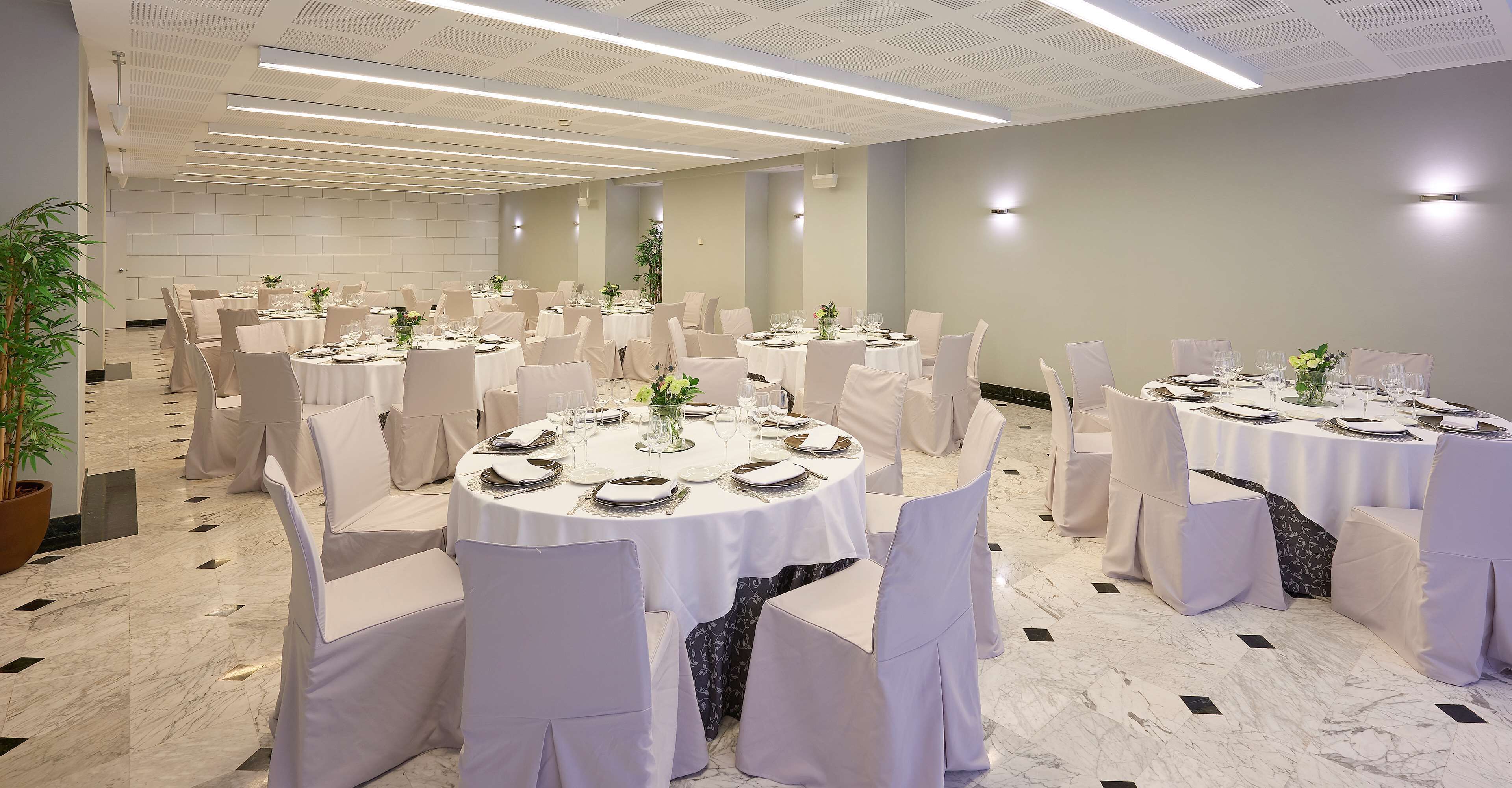 A banquet hall with round tables set for dining, white chairs, and a marble floor.