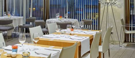 A restaurant with multiple tables set for dining, featuring white tablecloths, neatly arranged cutlery, and wine glasses.