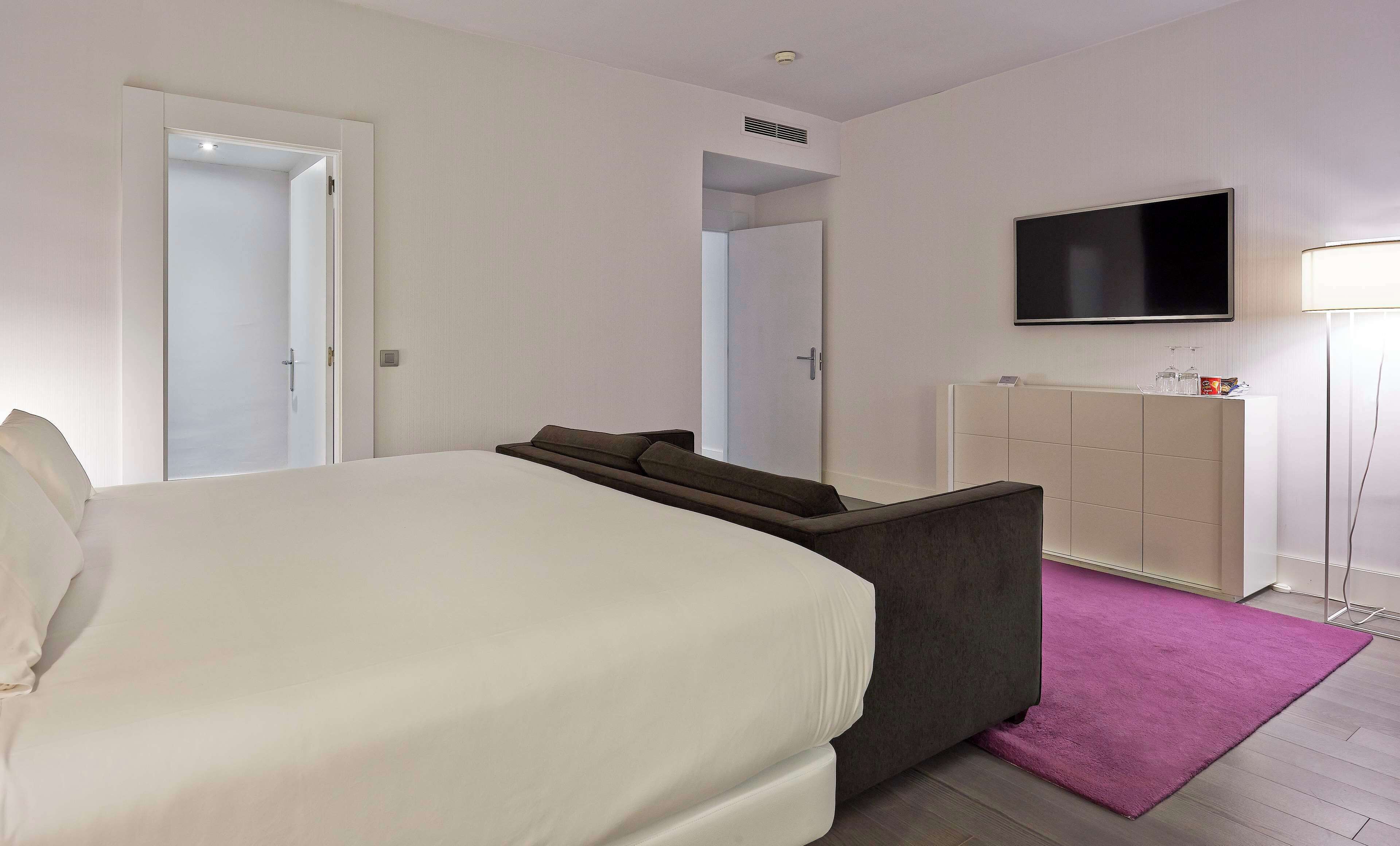 Una habitación de hotel con cama, sofá, televisor, armario y alfombra púrpura.