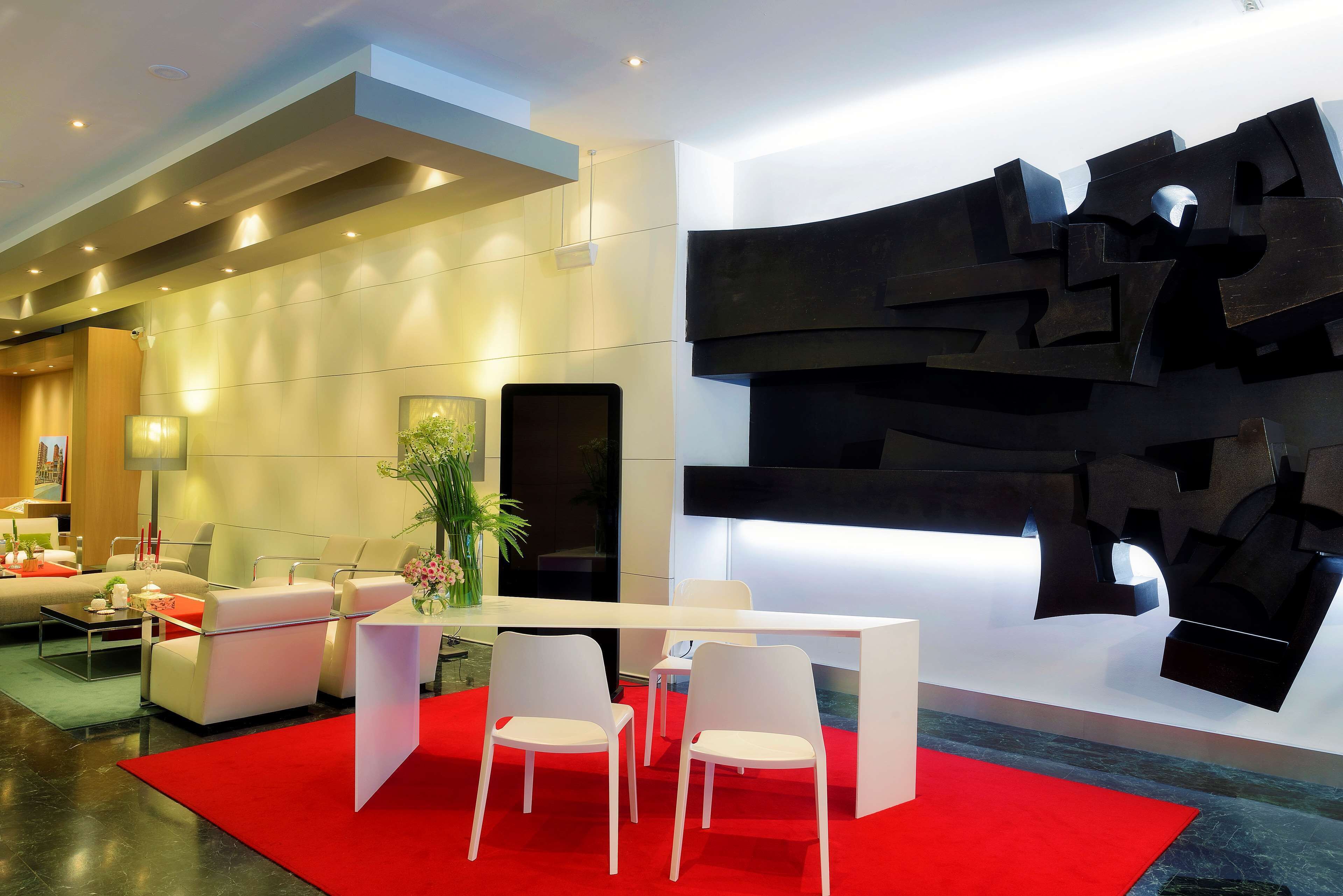 Rebost modern amb taulell de recepció, cadires blanques, una catifa vermella i una gran obra d'art abstracta a la paret.