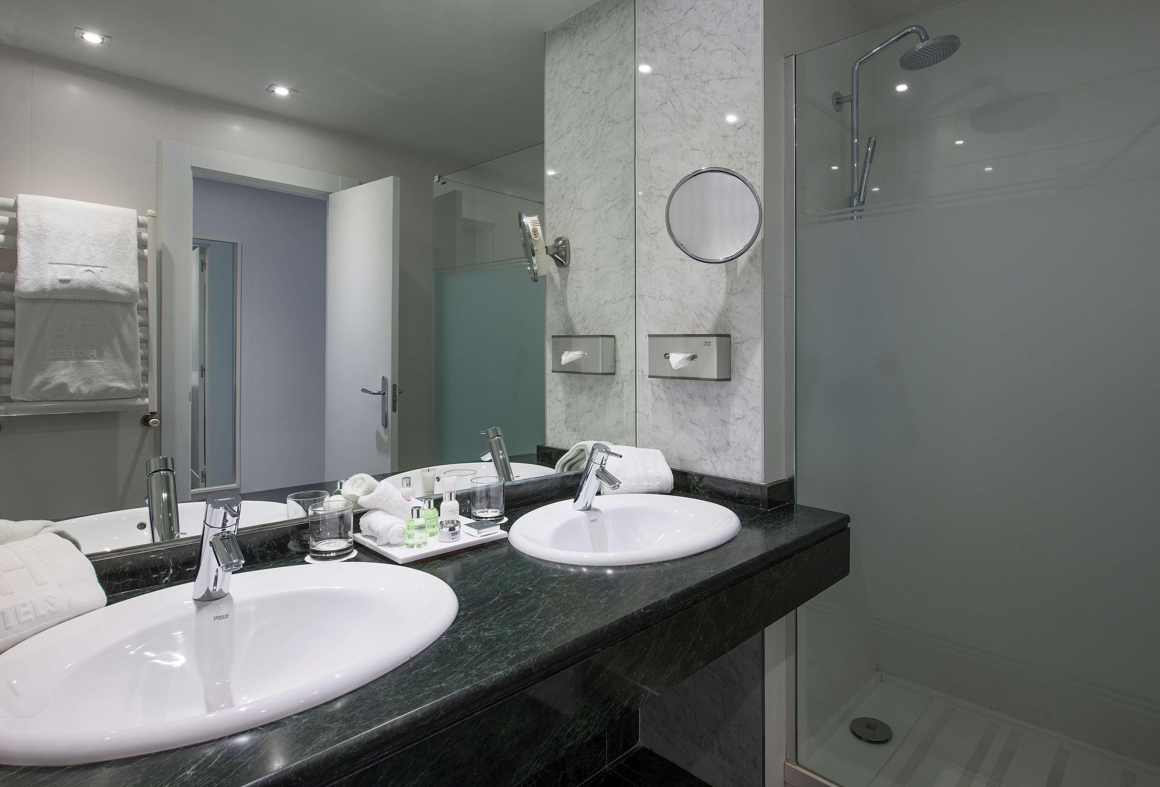 A modern bathroom with two sinks, a large mirror, and a glass-enclosed shower.