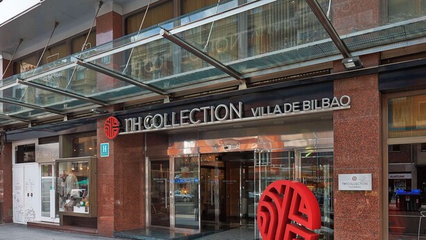 A hotel entrance with a glass facade, a prominent red logo, and a sign reading "TH COLLECTION VILLA DE BILBAO". - NH Collection Villa de Bilbao (Bilbao)
