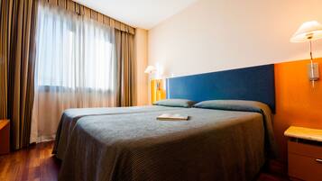 Habitación de hotel con una cama grande, dos lámparas de noche, una mesita de noche y una ventana con cortinas.