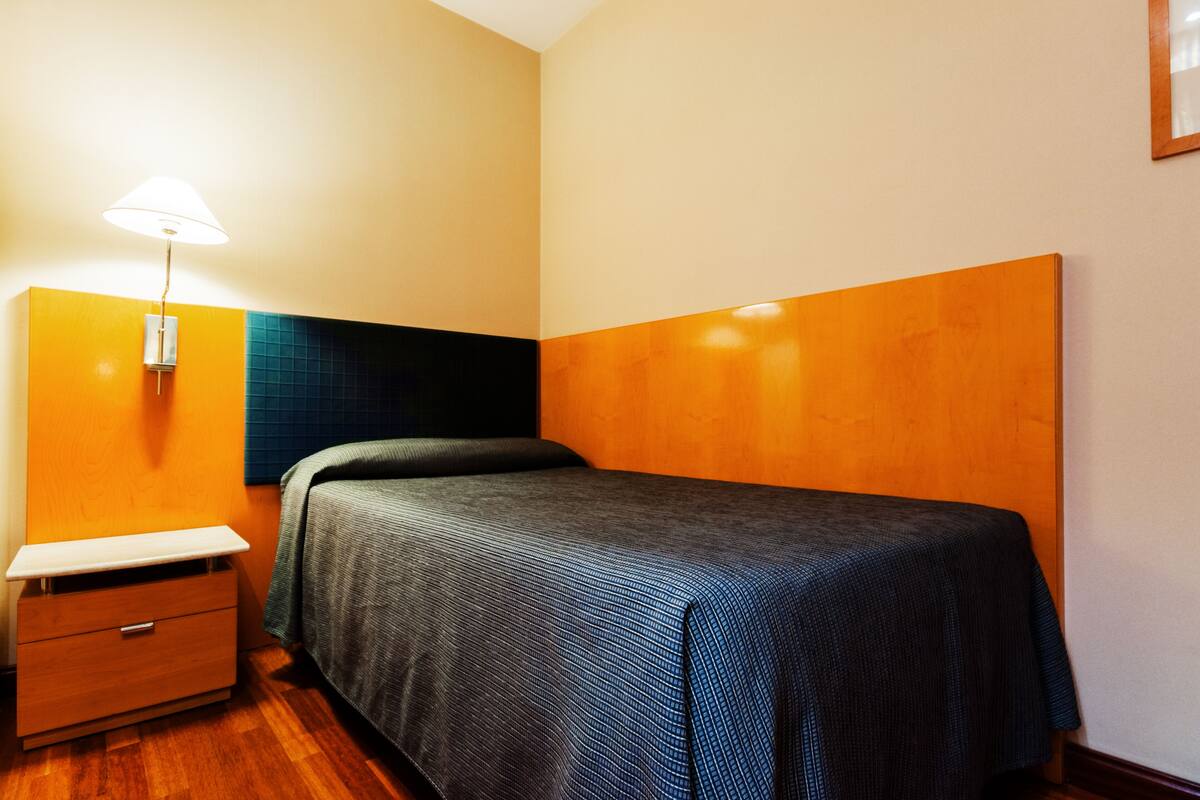 A small, neatly arranged bedroom with a single bed, a bedside table, and a lamp.