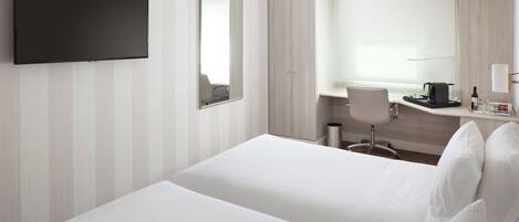 A hotel room with a large bed, a desk with a chair, a flat-screen TV, and a large mirror.