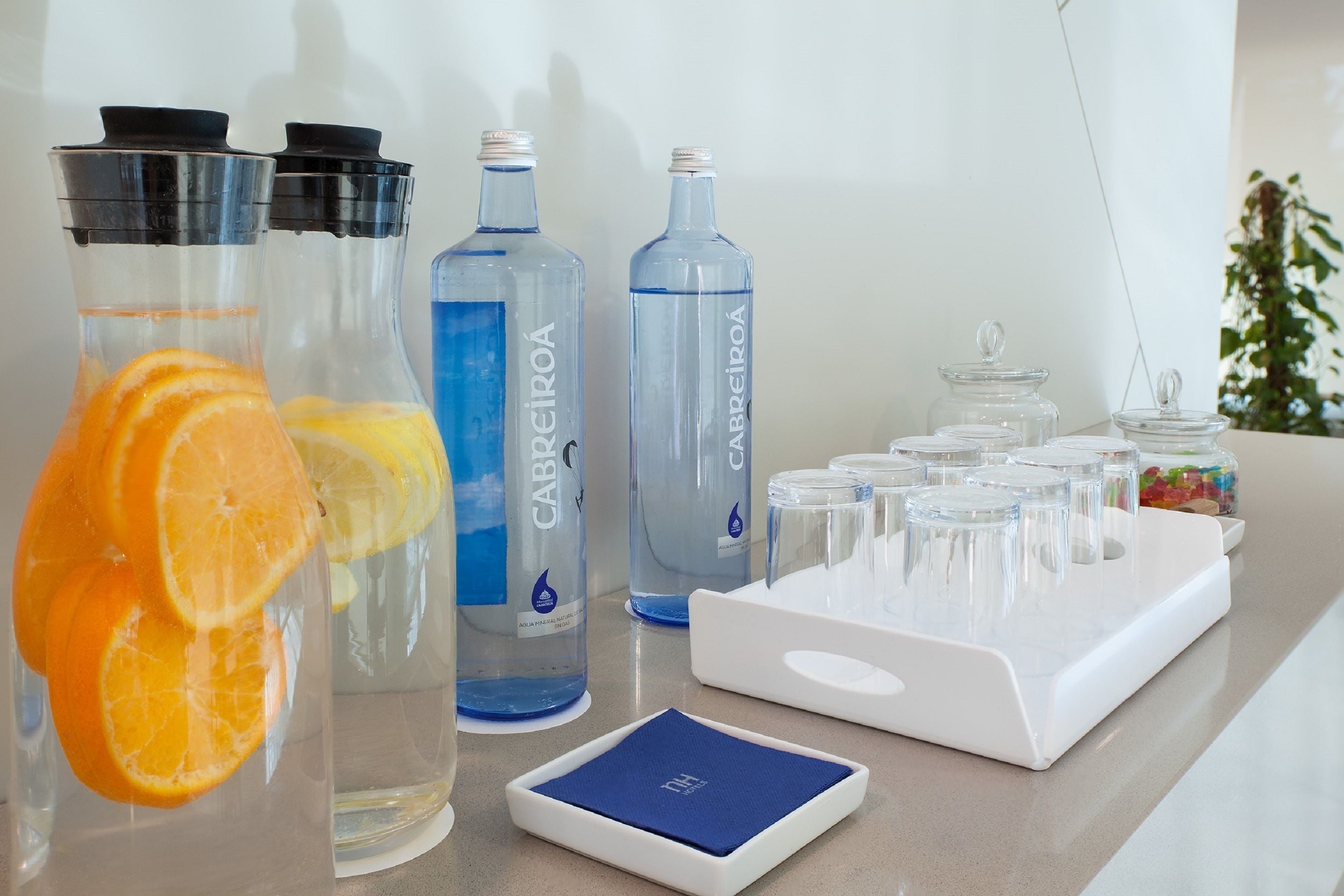 A counter with water bottles, a tray with glasses, and a plant in the background.