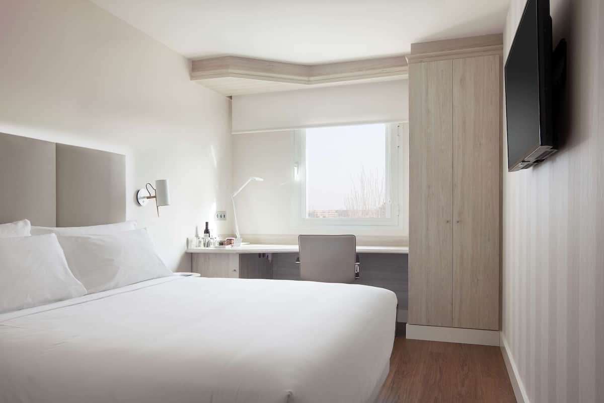 Een hotelkamer met een groot bed, een bureau met stoel, een aan de muur bevestigde televisie en een raam met uitzicht.