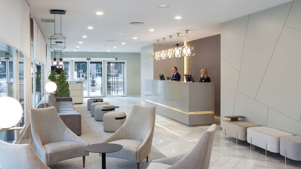 Een moderne lobby met een receptiebalie, een zithoek en grote ramen.