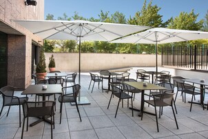 Una terrazza esterna con diversi tavoli e sedie, ampi ombrelloni e vasi con piante.