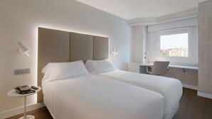 Een hotelkamer met een groot bed, nachtkastjes, een bureau en een raam met uitzicht op de stad.