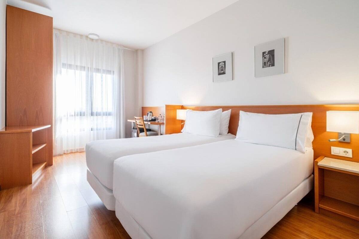 A hotel room with two beds, a desk, a chair, and a wardrobe.