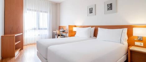 A hotel room with two beds, a desk, a chair, and a wardrobe.