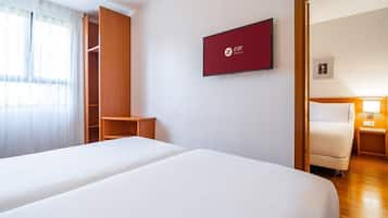 A hotel room with two beds, a wardrobe, a TV, and a nightstand with a lamp.