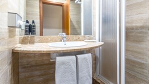 Un baño con lavamanos de mármol, un espejo y una cabina de ducha.