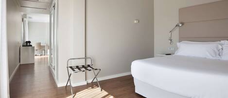 Una habitación de hotel con una cama grande, una mesita de noche, una lámpara y un perchero metálico.
