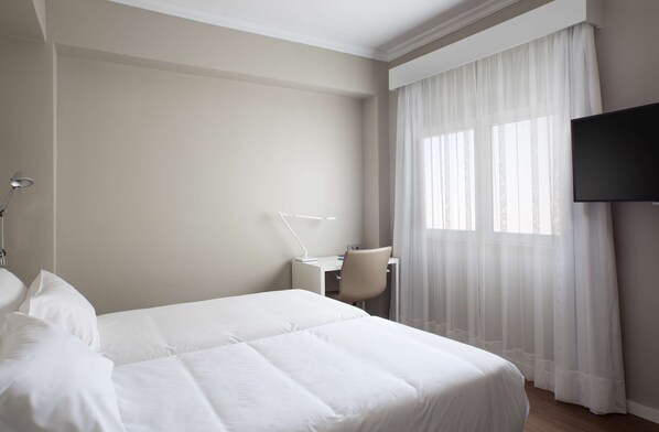 Habitación de hotel con una cama grande, un escritorio, una silla y un televisor.