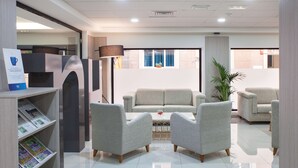 A modern hotel lobby with a sofa set, armchairs, a coffee table, and a bookshelf with magazines. - NH Las Palmas Playa las Canteras (Las Palmas de Gran Canaria)