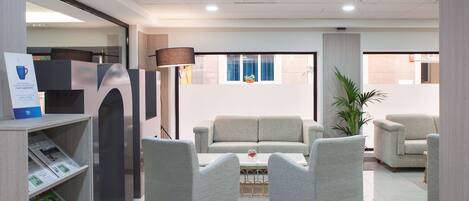 Un hall d’hôtel moderne avec un ensemble de canapés, des fauteuils, une table basse et une bibliothèque contenant des magazines.