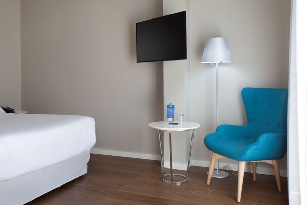 Una habitación de hotel con cama, una mesita redonda con lámpara y una silla azul.