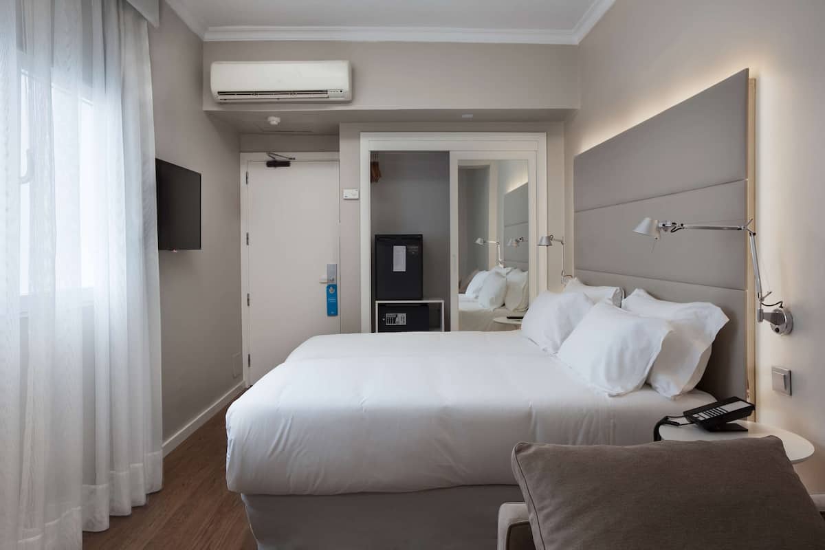 Une chambre d’hôtel avec un grand lit, une table de chevet avec une lampe, un téléviseur fixé au mur et un appareil de climatisation.