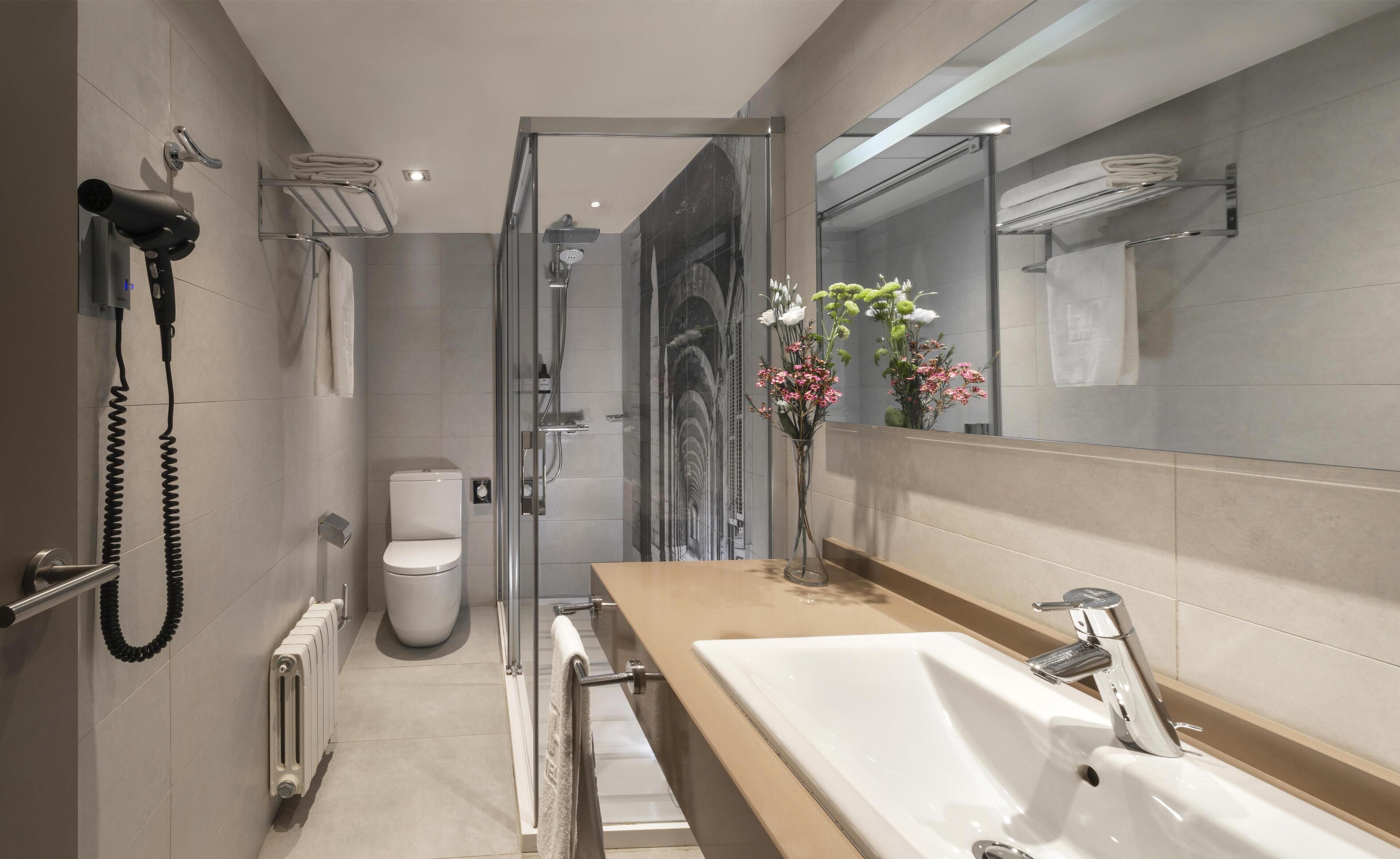 A modern bathroom with a large mirror, a white sink, a glass shower enclosure, and a toilet.