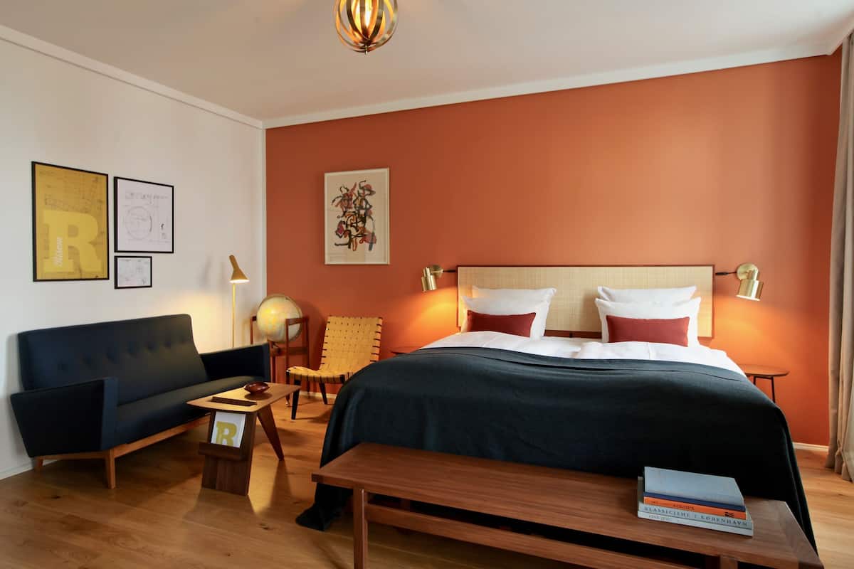 A hotel room with a bed, a sofa, a chair, a small table, and a bench.