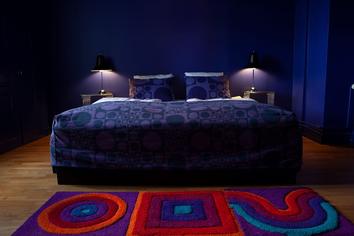 A bedroom with a bed, two bedside lamps, and a colorful rug.