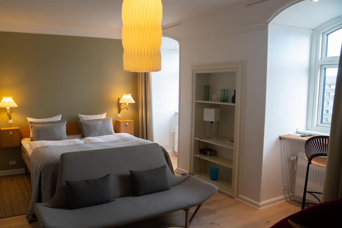 A bedroom with a bed, bedside lamps, a bench, and a bookshelf.