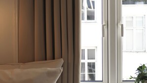 A hotel room with a bed, a window with curtains, a radiator, and a small table with a book. - Hotel Alexandra (Copenhagen)