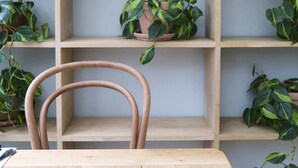 A wooden table with two clear glasses and a chair in front of a shelving unit with potted plants. - Hotel Alexandra (Copenhagen)