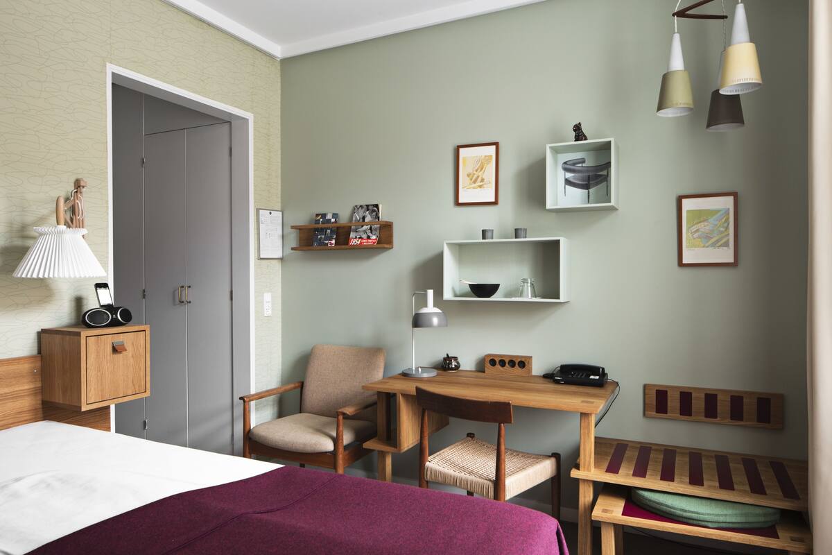 A hotel room with a bed, desk, chair, and shelves with pictures and items.