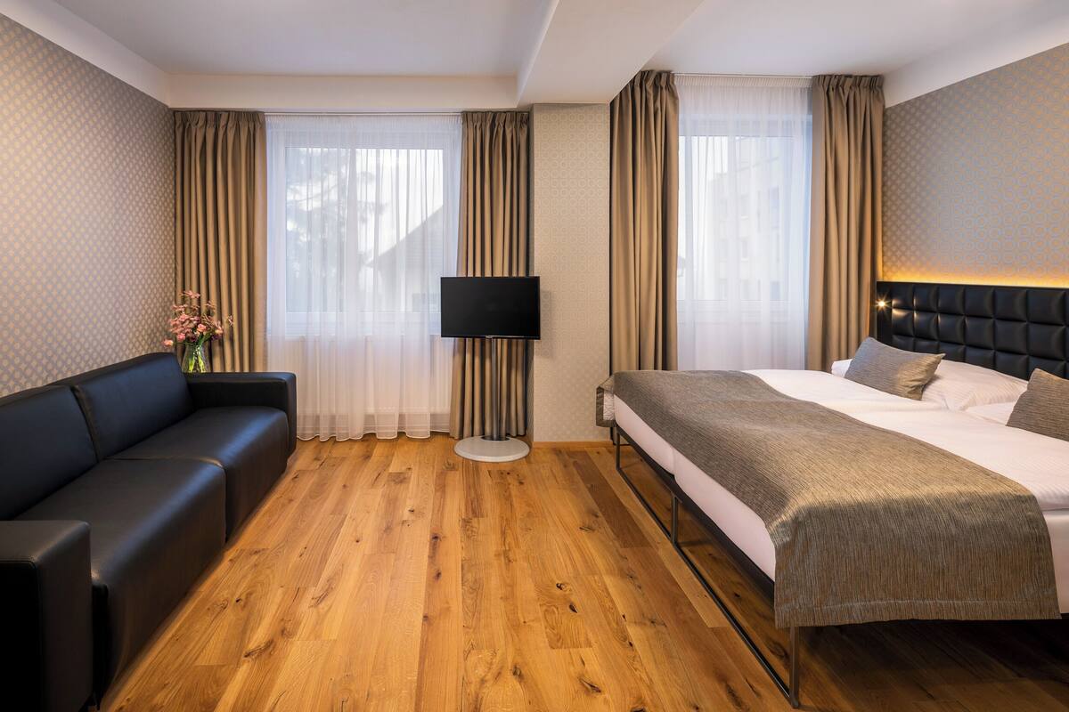 Una habitación de hotel con cama, sofá, televisión y lámpara.