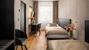 A hotel room with two beds, a desk, a chair, and a vase with flowers. - Aida Hotel (Prague)