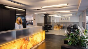 A modern reception area with a marble counter, black seating, and large windows. - Aida Hotel (Prague)