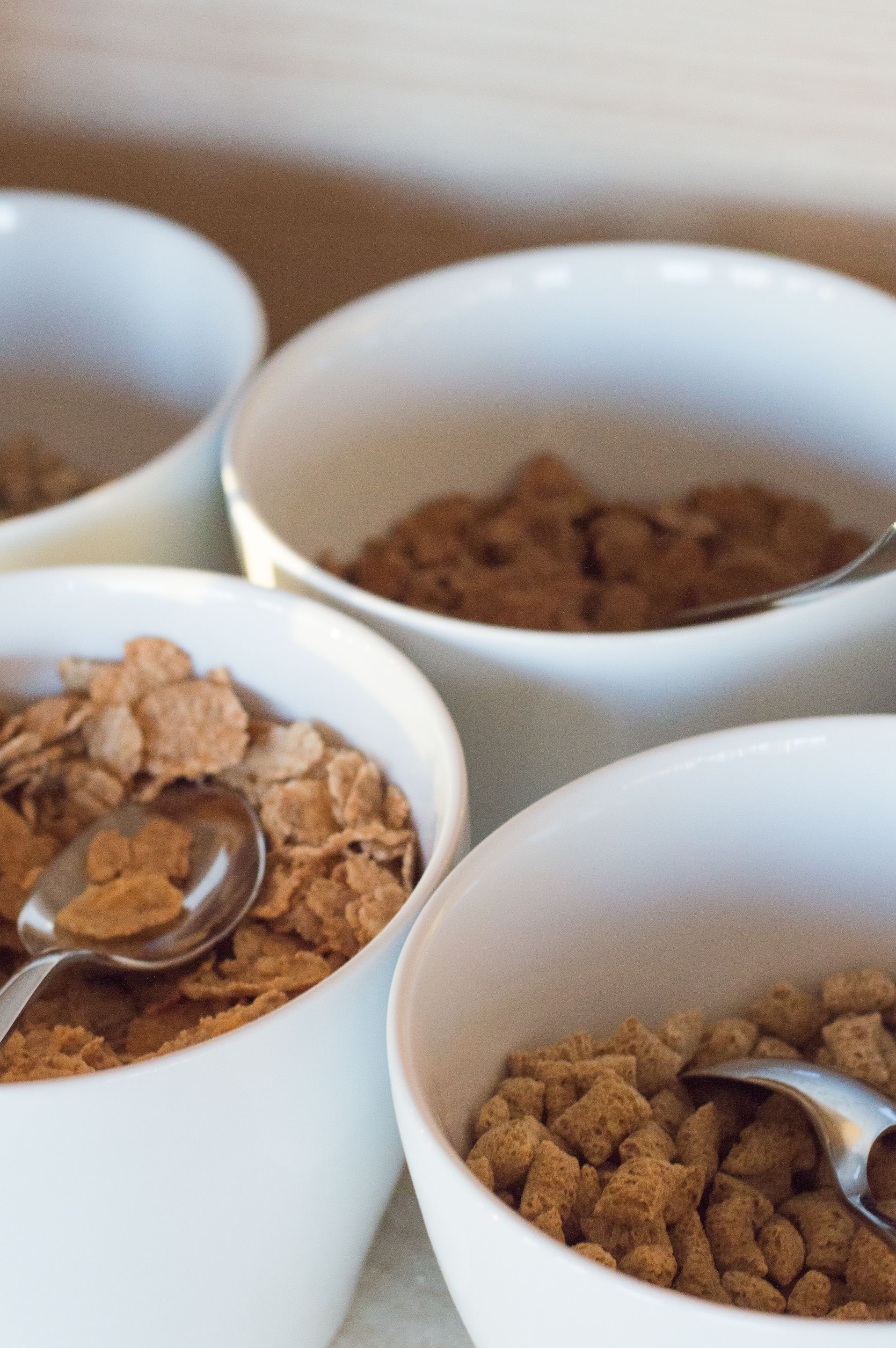 Four white bowls containing cereal flakes, each with a spoon.