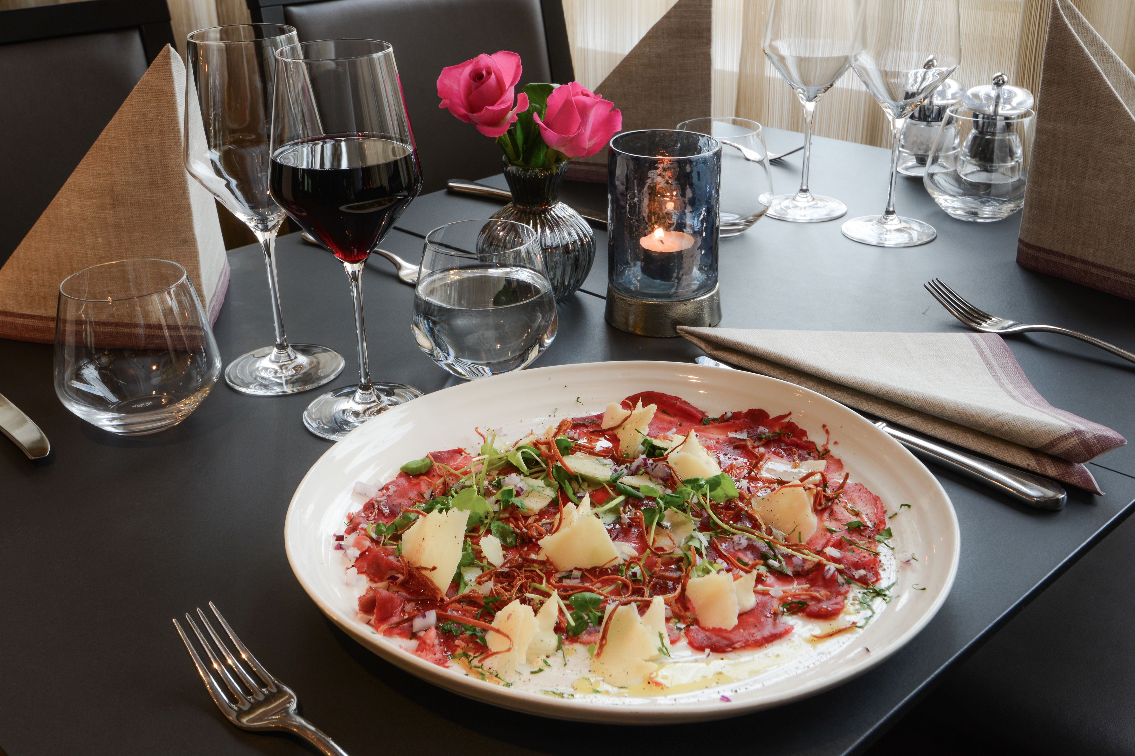 A dining table set with a plate of food, wine glasses, and a candle.