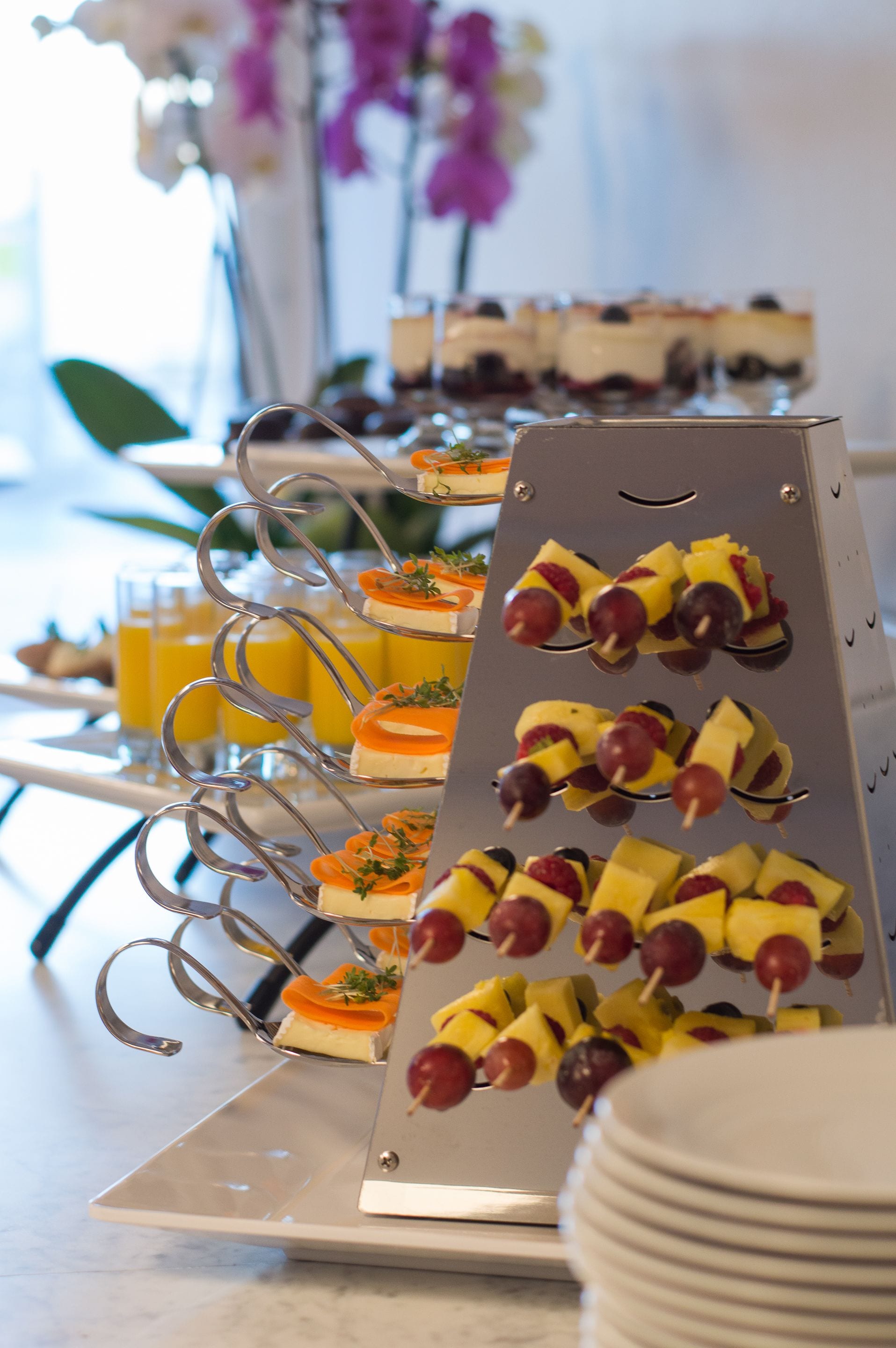 En buffetbord med forskellige retter, herunder frugtspyd og desserter.