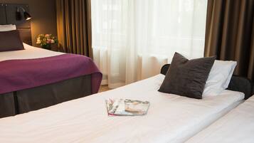 Una habitación de hotel con una cama, una mesita de noche con lámpara, una ventana con cortinas y un jarrón con flores.
