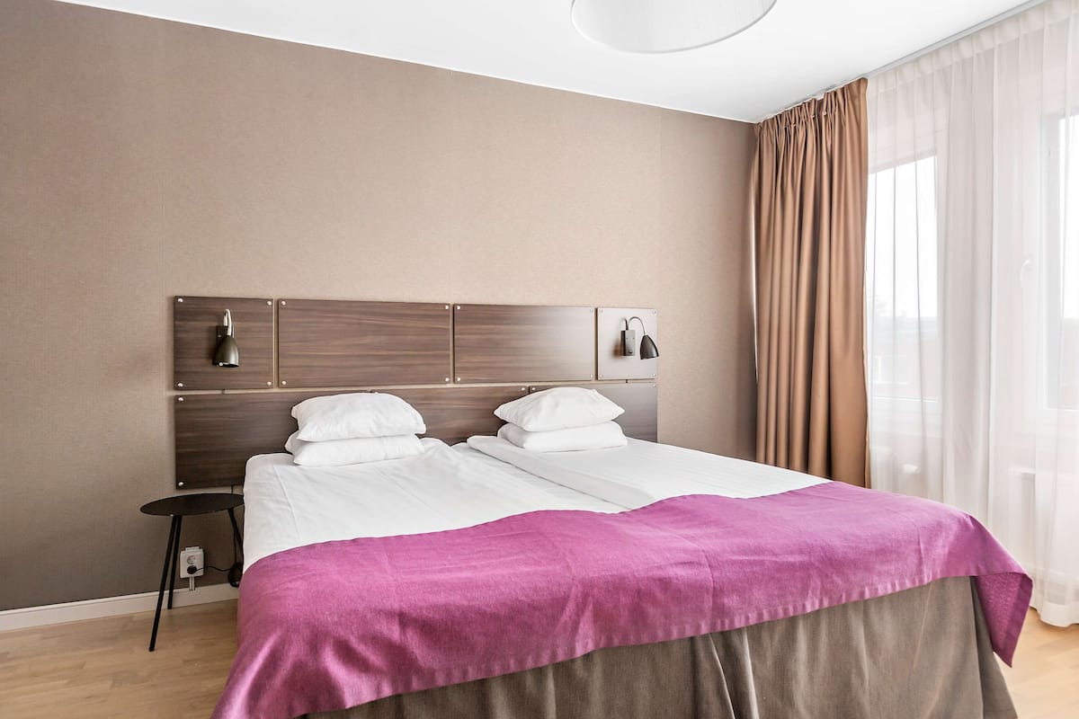 A double bed with a wooden headboard, two bedside lamps, and a purple bedspread.