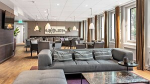 A modern hotel lobby with a grey sofa, dining area, and large windows. - Best Western Arlanda Plus Park Airport Hotel (Arlandastad)