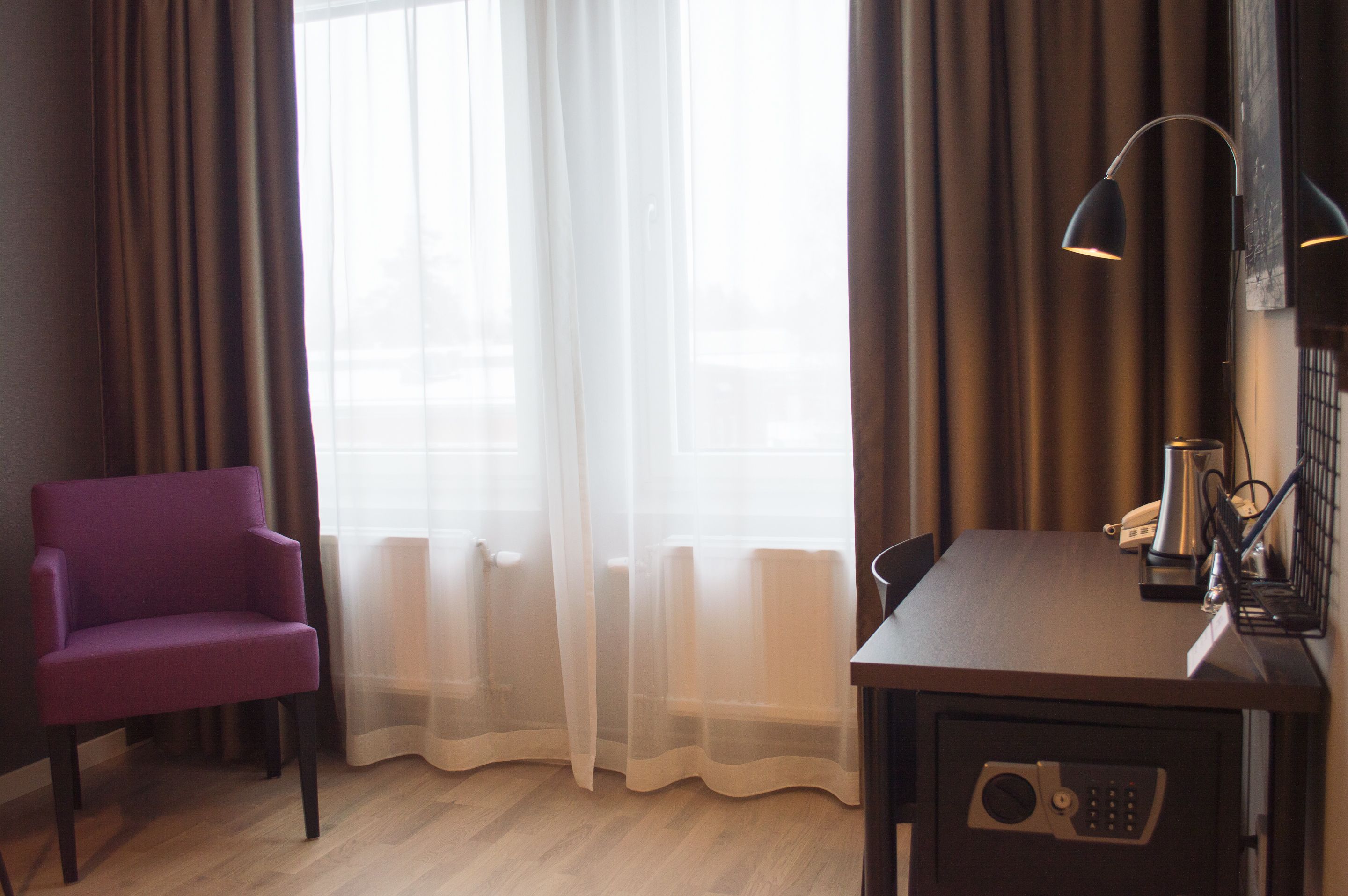 Una habitación con una silla morada, un escritorio con una lámpara y un radiador.