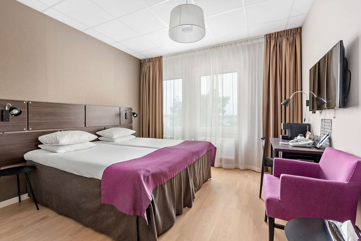 A hotel room with a large bed, a desk with a computer, a chair, and a TV on the wall.