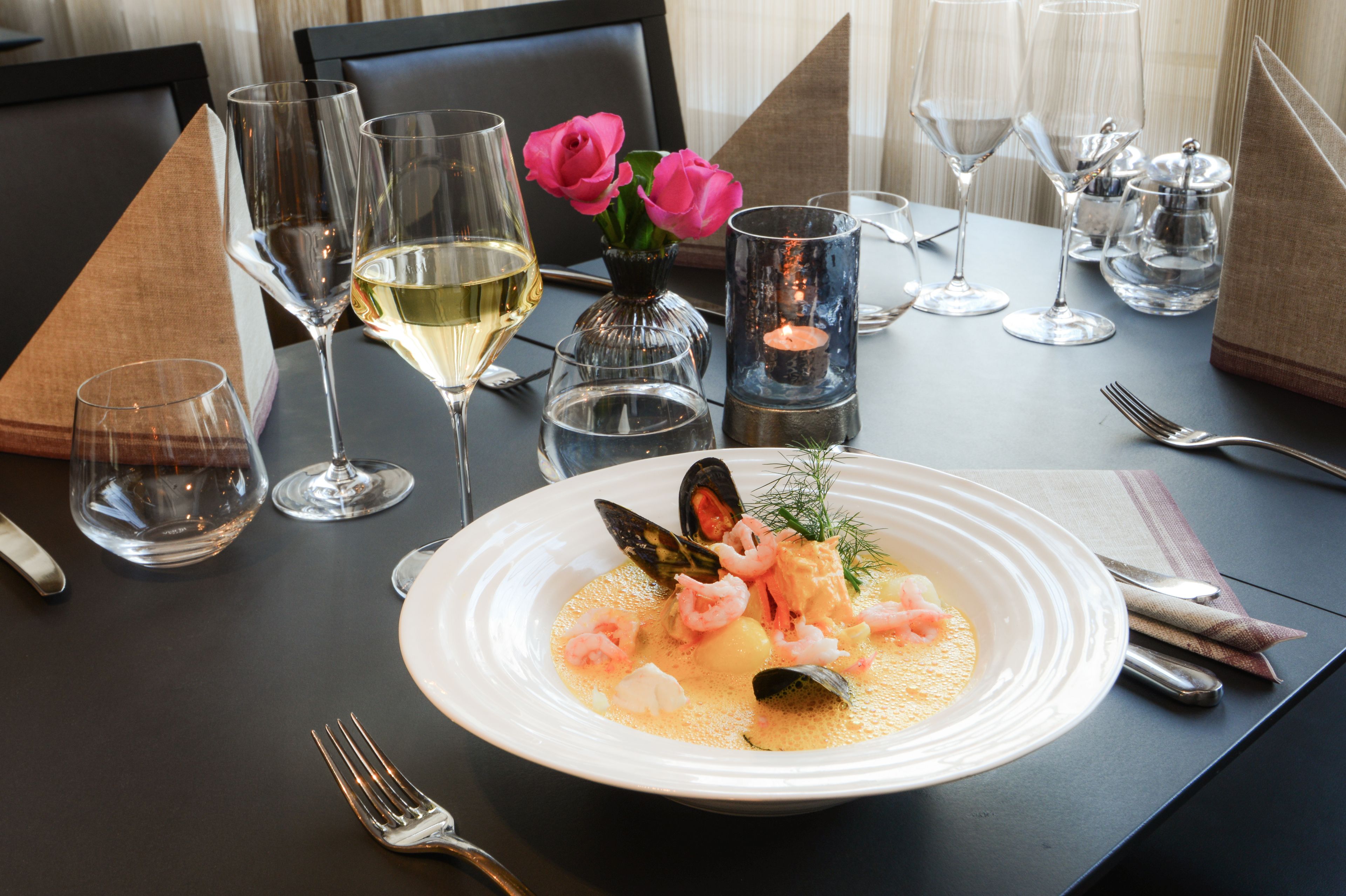 A dining table set with a seafood dish, wine glasses, and a candle.