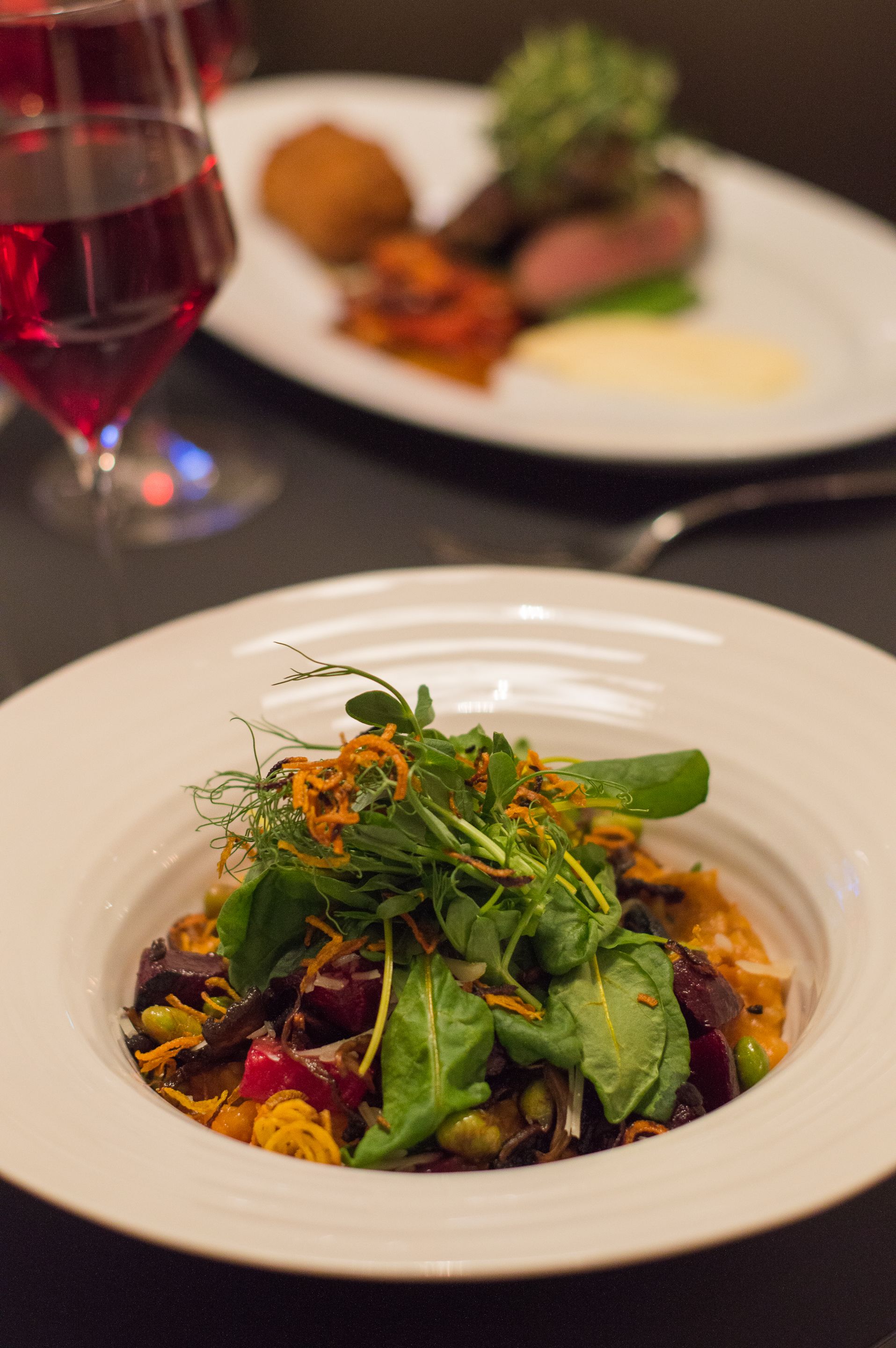 A dining table with a white plate of salad and a glass of red wine.