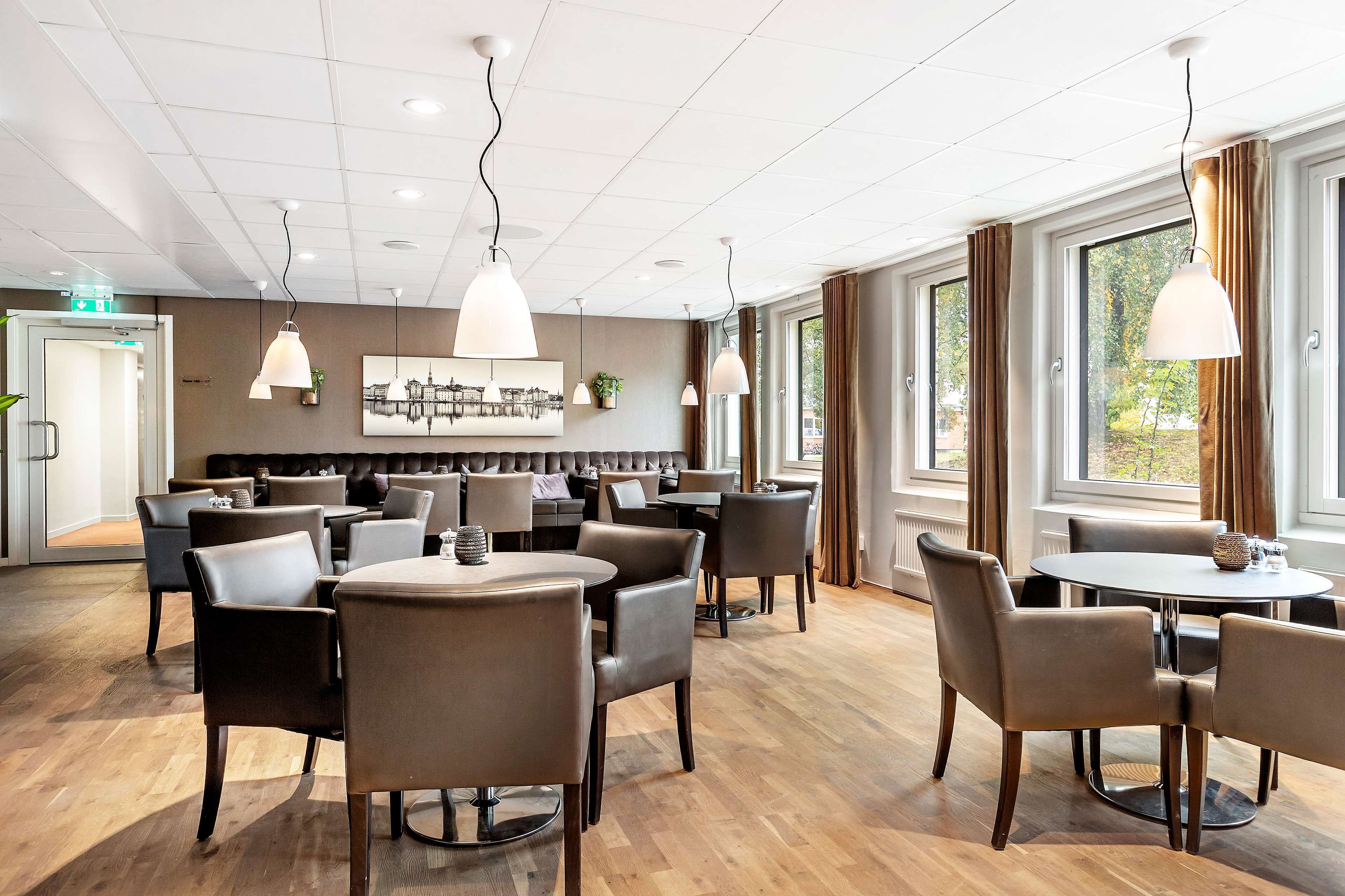 A modern dining area with round tables and chairs, pendant lighting, and a view of the outdoors through large windows.
