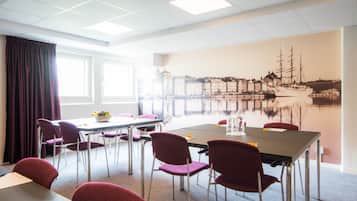 Un salón de conferencias con una gran mesa, sillas rojas y un mural que representa una escena portuaria.