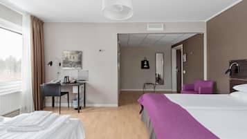 A hotel room with a bed, a desk with a phone, a chair, a purple armchair, and a window with curtains.