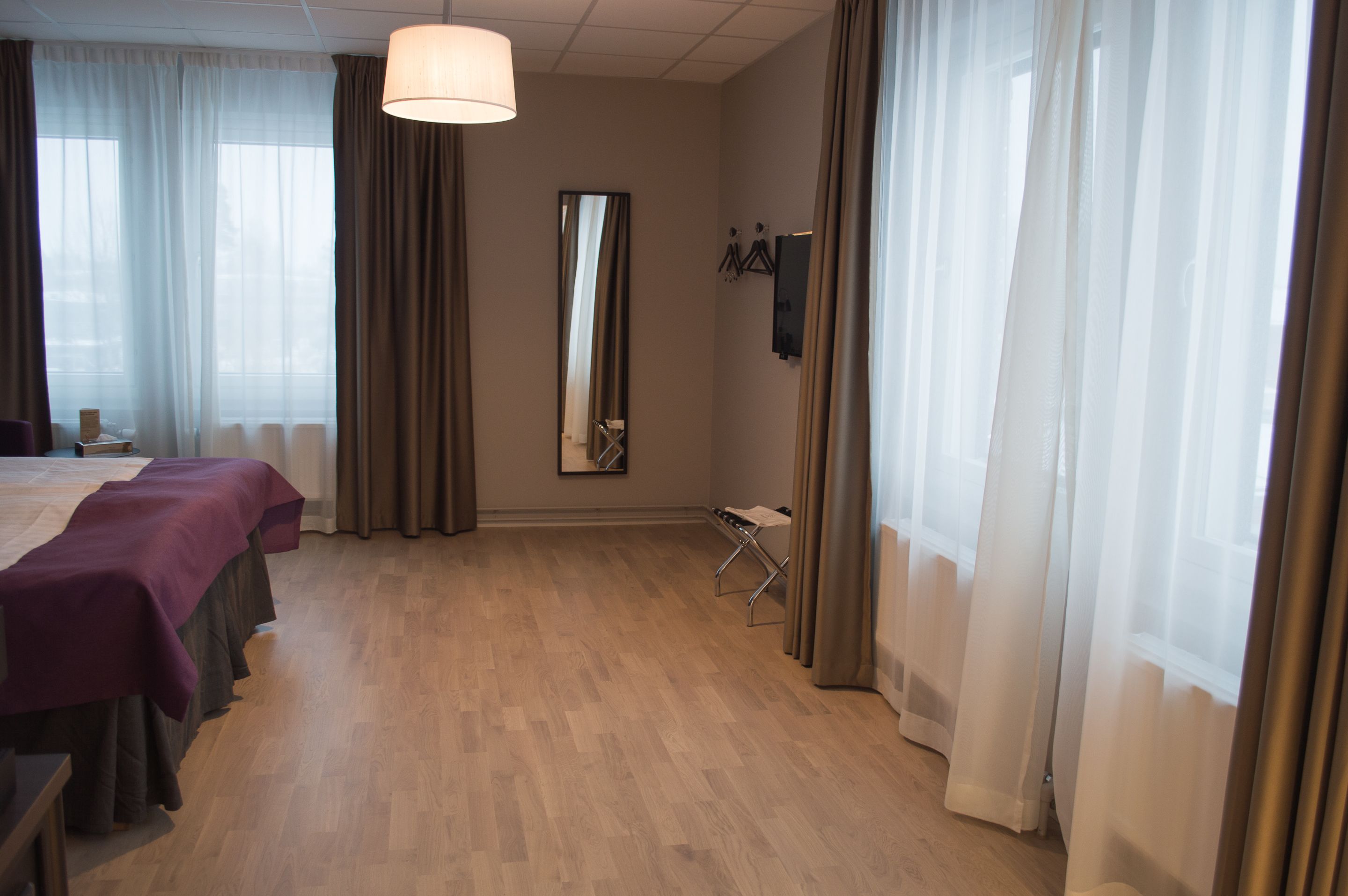 Hotellihuone, jossa on suuri sänky, työpöytä, tuoli, peili ja ikkuna, jossa on verhot.